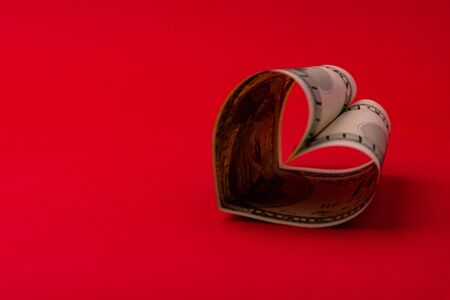 Heart made of dollar bill on a red background