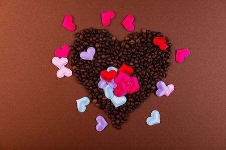 Coffee beans on a dark background. Coffee beans in the shape of a heart. Colored hearts on top.の写真素材