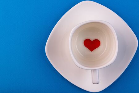 White cup of coffee on a blue background with a heart-shaped candy. Valentine's Dayの写真素材