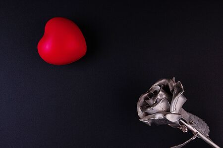 A thin bronze rose made by forging from metal. Red volumetric heart nearby.の写真素材