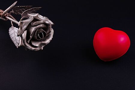 A thin bronze rose made by forging from metal. Red volumetric heart nearby.