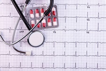 A stethoscope and pills lie on a cardiogram. Healthcare, cardiology and media concept.の写真素材