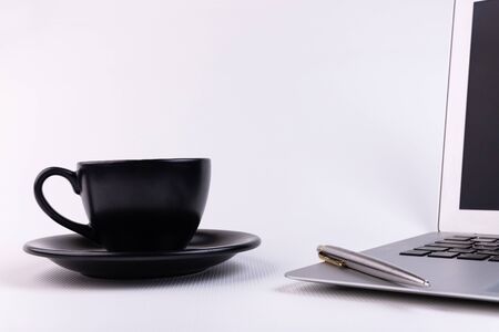 White office desk desk with computer, pen and black cup.