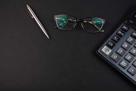 Glasses, pen and calculator on a black background