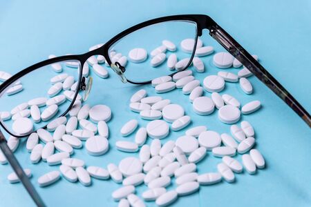 White scattered pills and glasses on a blue backgroundの写真素材
