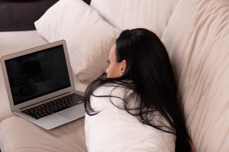 Young woman lying on a sofa watching a movie on a laptopの写真素材