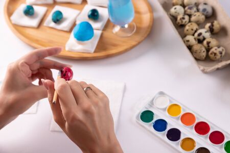 easter, holidays, tradition and people concept - close up of woman hands coloring easter eggs with...