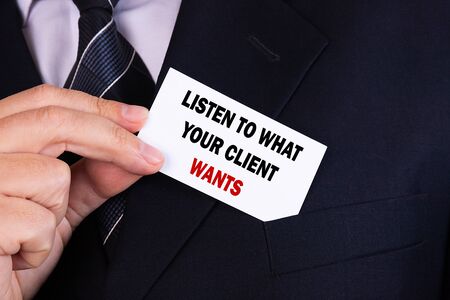 Businessman putting a card with text WHAT YOUR CLIENT WANTS in the pocketの写真素材