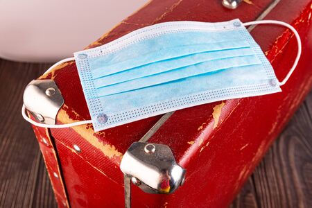 Close-up - a medical disposable mask is lying on a suitcase as an unsuccessful journey. Concept.