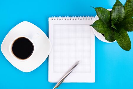 Open a blank white notebook, with pen, flower and a cup of coffee on a blue table. Business conceptの写真素材