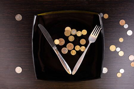 The rise in price of food, the crisis. Coins instead of food in a black plate with cutlery. Business concept.の写真素材