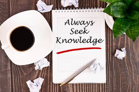 Always seek knowledge, an inscription in a notebook on a wooden table with a pen and a cup of coffee.の写真素材