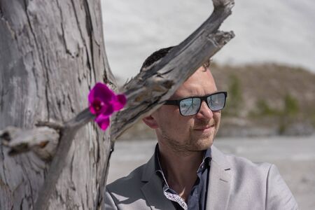Ecological concept. A businessman stands next to a dry tree on which a live flower grows against the...