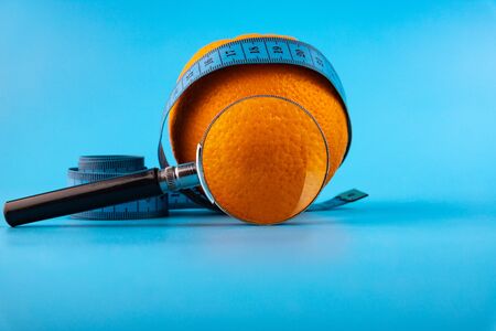 Fresh orange with a magnifying glass on a blue measuring tape - diet, fitness, lifestyle, healthy and vegetarian conceptの写真素材