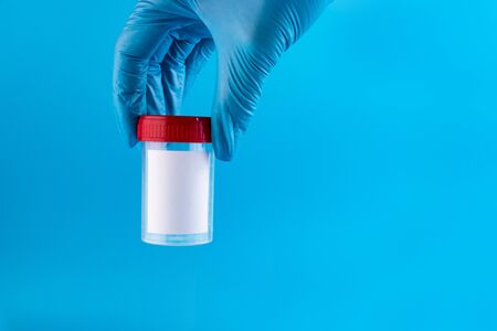 Hands of a doctor or nurse in blue gloves holding an empty analysis container on a blue background.