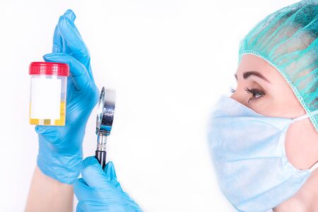 Doctor examines a container with a urine test through a magnifying glass on a white background.の写真素材