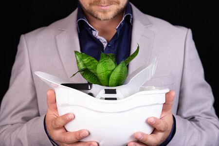 Businessman, engineer holds in his hands a white building helmet from which a plant sprout sprouts. Money growth concept. Ecology concept. Concept Save the world.の写真素材