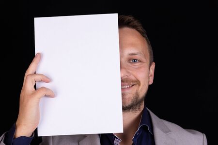 A man in a gray suit holds a blank sheet of paper with place for text in his hands on a black background. Business idea, concept.の写真素材