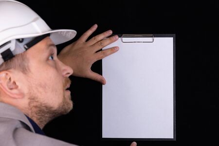 Engineer, builder, businessman in a white helmet on a dark background holds a white tablet in his...