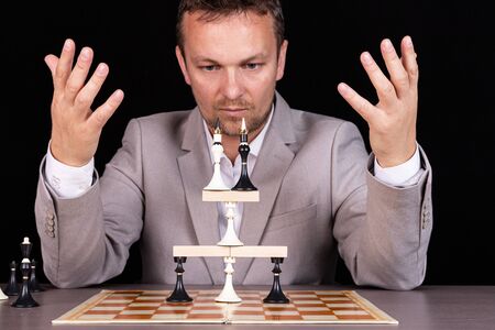 A businessman is building a pyramid of chess pieces and wooden blocks. The concept of construction,...