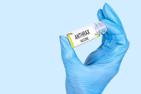 ANTHRAX VACCINE text is written on a vial whose ampoule is held by a hand in a medical disposable glove. Medical concept.の写真素材