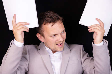 Frustrated and annoyed businessman with angry emotion on his face with papers in his hands. Business concept.の写真素材