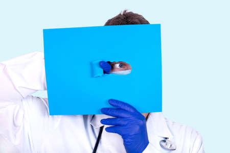 Doctor proctologist looks out from under excerpts of a paper sheet. Medical conceptの写真素材