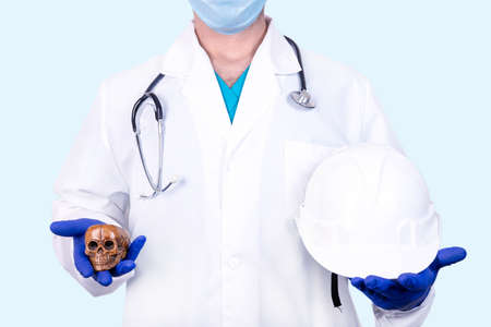 Industrial Safety Concept. The doctor holds a construction helmet in one hand and a human skull in the other.の写真素材