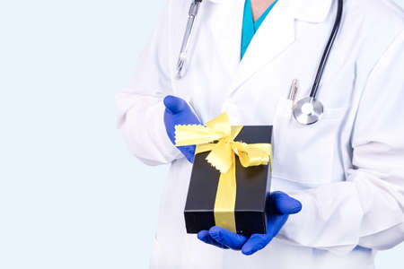 Chronic disease medical concept. A doctor in medical clothes holds a black gift tied with a yellow ribbon.の写真素材