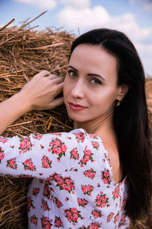 Beautiful dark-haired girl in a summer dress on a background of hay, nature.