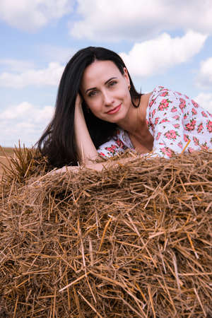 Beautiful dark-haired girl in a summer dress on a background of hay, nature.の写真素材