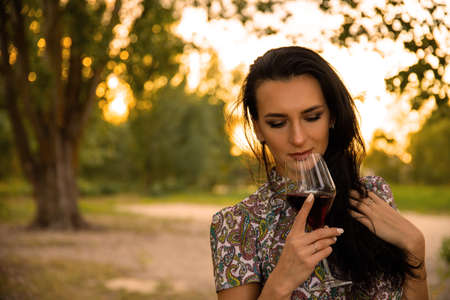 Sexy, young, attractive girl, woman, with a glass of red wine on a background of nature and sunset.の写真素材