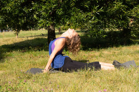 Female fitness instructor does, shows exercises in a green park. Sport concept.