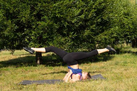 Female fitness instructor does, shows exercises in a green park. Sport concept.