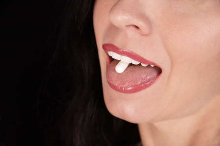 White oval tablet, capsule on the tongue of a girl, woman, close-up. Placebo concept.