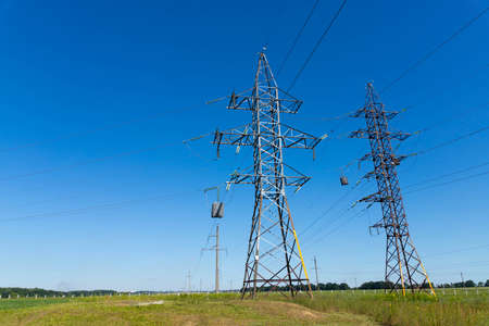 a high voltage power pylons against blue sky and sun raysの写真素材