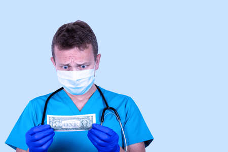 Portrait of a young handsome doctor with one dollar banknote on a light background. Medical salary...