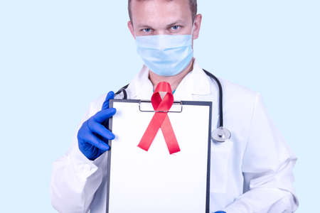 A doctor in medical gloves holds a tablet with a red ribbon - a symbol of the fight against AIDS and vasculitis and a place for text.の写真素材