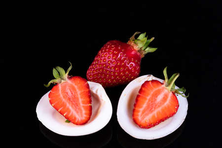 Red strawberry in a shell on a black background. Sweet life concept. Selective focus