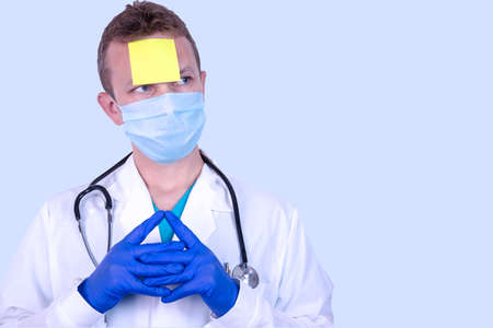 Doctor with an empty yellow sticky reminder prielyinom to his forehead. The concept of ethics and reminders of wearing a medical, protective disposable mask in public places.の写真素材