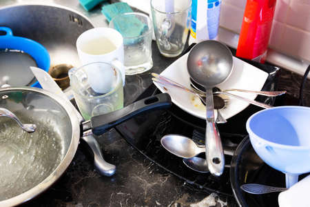 A pile of dirty dishes in the metal sink and on the table is pouring. Kitchen after breakfast, lunch, dinner. Clean dishes concept.の写真素材