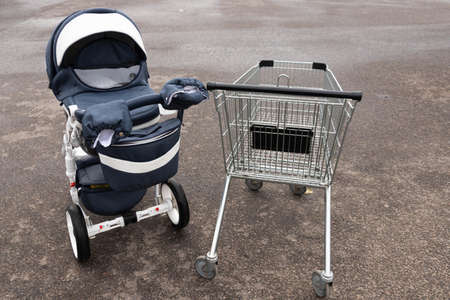 An empty grocery cart from a supermarket on the street and a baby carriage. Concept.