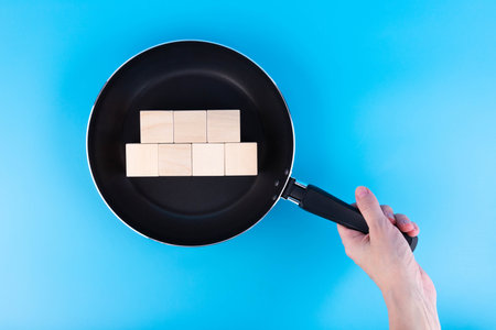 Hot news concept. Hand holds a frying pan with wooden cubesの写真素材