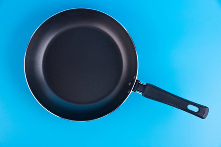 Black metal frying pan on a blue background.の写真素材