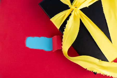 Black gift box with gold satin ribbon on red background.の写真素材