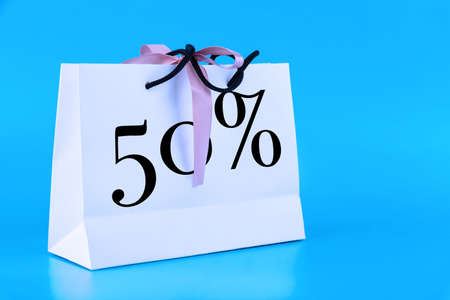 White paper bag, shopping bag with 50 percent sign on blue background. Copy space.の写真素材