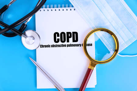 COPD Chronic obstructive pulmonary disease, text written in a notebook lying on a blue background, with a stethoscope and a medical mask. Medical concept.の写真素材