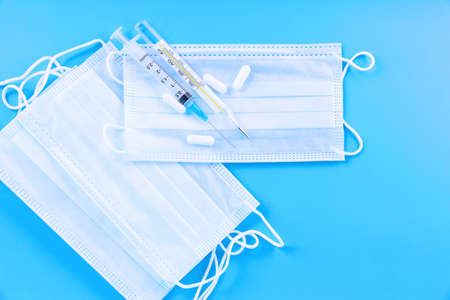 Medical protective mask with pills, thermometer, medicines, syringes on blue desk. Dangerous virus . Healthcare and medical concept.の写真素材