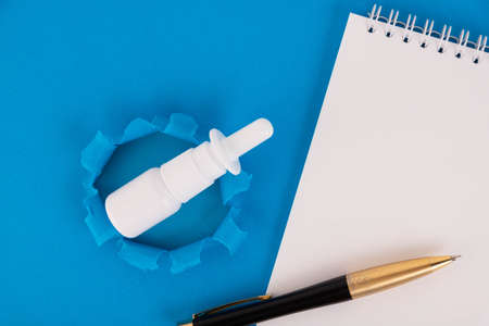 Medicine bottle, nasal spray, notebook with pen. Seasonal illness concept. Nasal medicines, copy space, on a blue isolated background.の写真素材