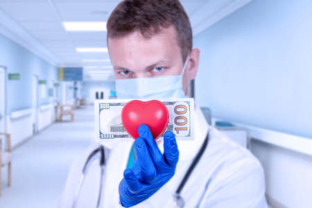 Life insurance concept. The doctor holds a red heart and a hundred dollar bill. Selective focus